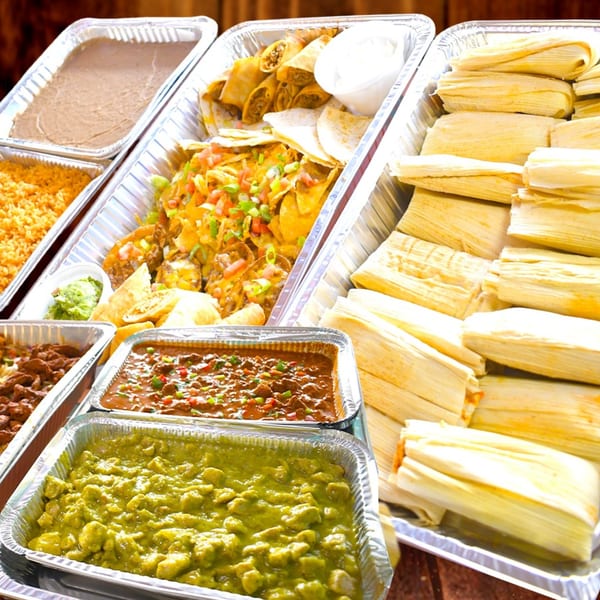 A catering spread of Mexican food including tamales, nachos, rice, beans, and various stews.
