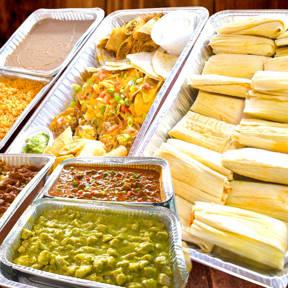A catering spread of Mexican food including tamales, nachos, rice, beans, and various stews.