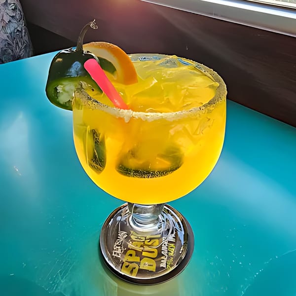 A vibrant yellow margarita with a salted rim, garnished with a jalapeño and orange slice.