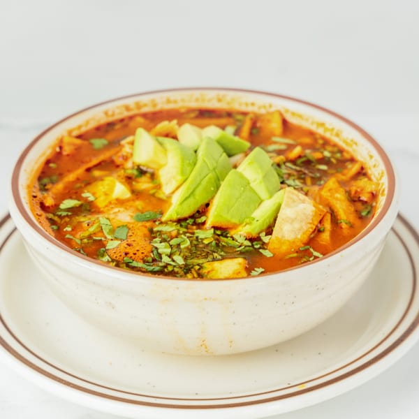 A bowl of Juan Colorado's Mexican tortilla soup, garnished with avocado slices and fresh cilantro.