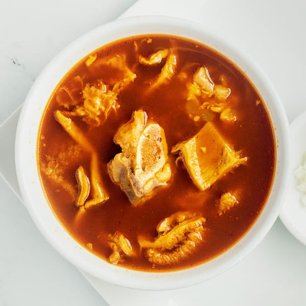 Overhead view of a bowl of menudo, a traditional Mexican tripe soup with red broth.