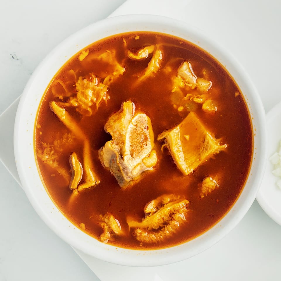 Overhead view of a bowl of menudo, a traditional Mexican tripe soup with red broth.