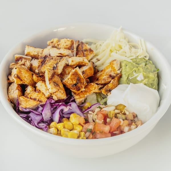 A vibrant Mexican chicken bowl with grilled chicken, red cabbage, corn, pico de gallo, guacamole, and sour cream.