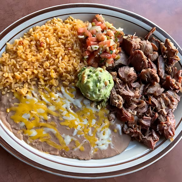 A Mexican dish with rice, refried beans with cheese, carnitas, pico de gallo, and guacamole.