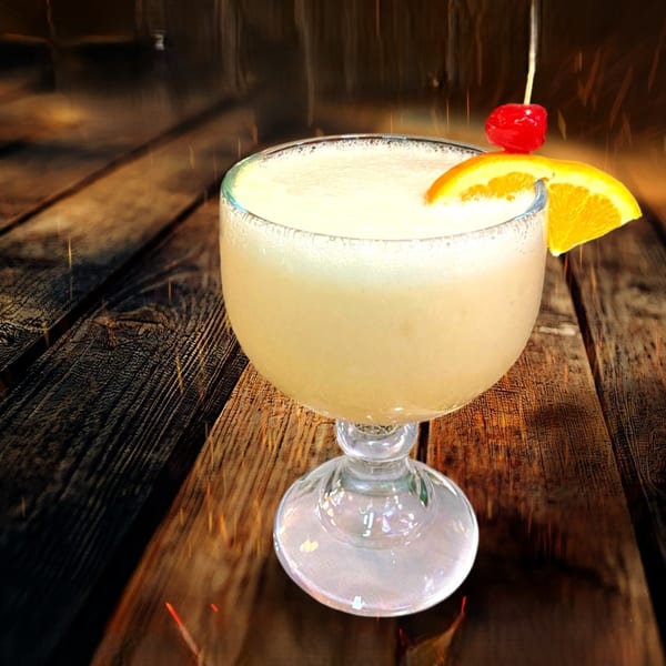 A frozen margarita in a goblet, garnished with an orange slice and a cherry, on a wooden table.