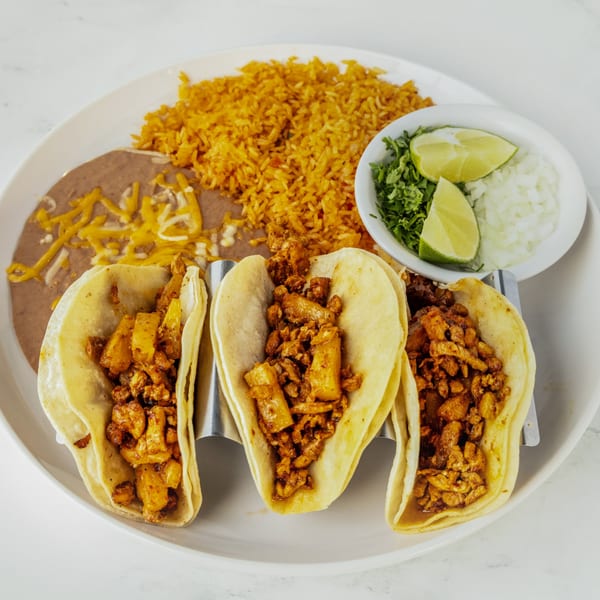 Three al pastor tacos with rice, refried beans, and a side of cilantro, onions, and lime.