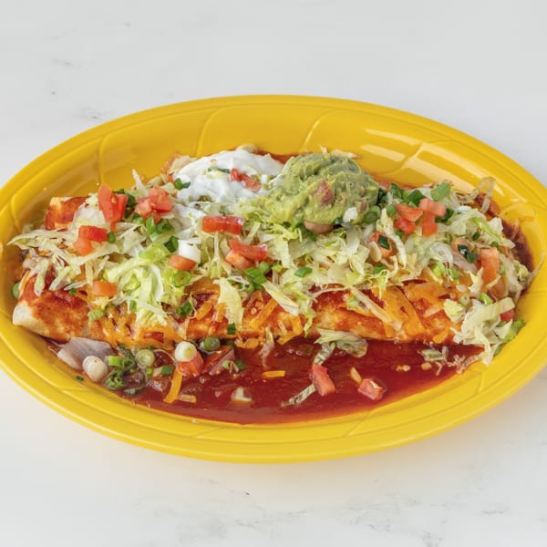 A Juan Colorado Restaurant burrito covered in red sauce, cheese, lettuce, tomatoes, sour cream, and guacamole.